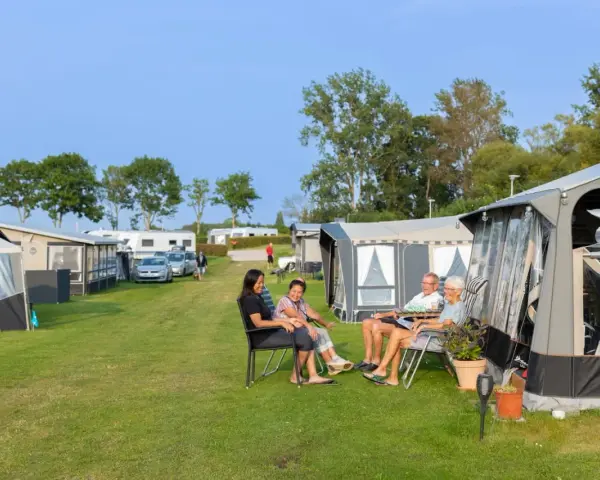 Familj njuter av en solig dag på en av Sveriges billiga campingar. Husvagnar och tält står uppradade på en grön gräsmatta.