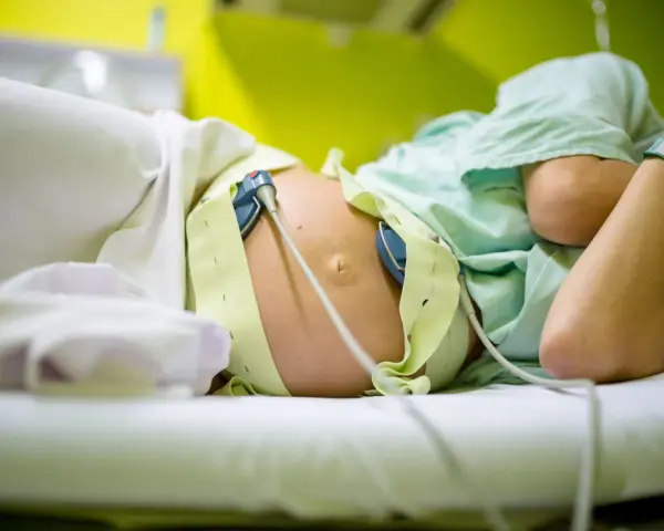 Kobieta w ciąży leży na łóżku, podłączona do aparatury KTG. Czekając na rozwój wydarzeń.