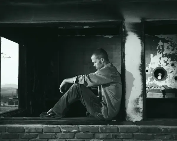 A man sits in a doorway, contemplating what the Bible says about complaining. The scene is stark and desolate, reflecting a mood of introspection.