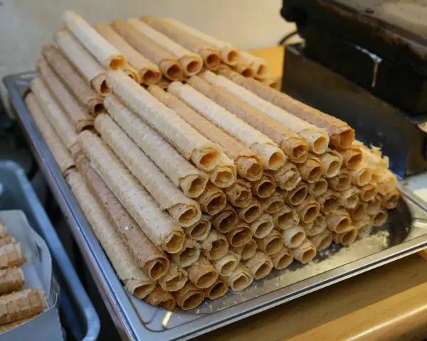 Stos kupnych wafli do rurek z kremem, obok gorącej gofrownicy.