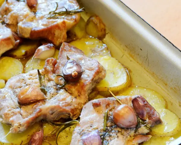 Pieczona karkówka z ziemniakami, czosnkiem i rozmarynem w naczyniu żaroodpornym.