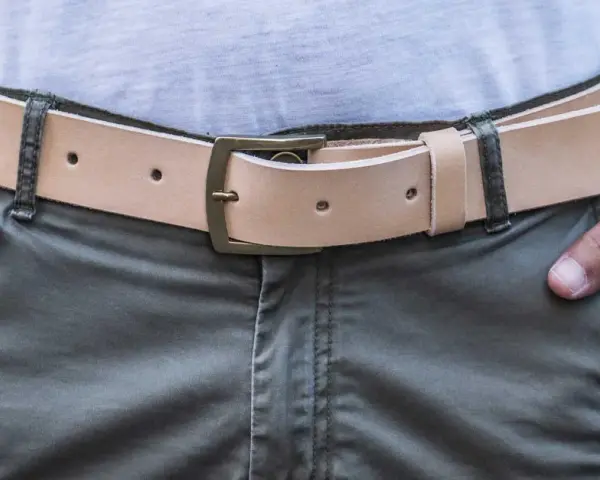 Cintura in cuoio chiaro con fibbia in ottone, indossata su pantaloni verdi. Si vede da che lato si mette la cintura.