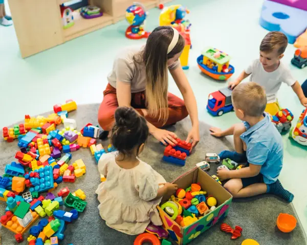 Dzieci bawią się klockami z opiekunką. Czy za żłobek się płaci? To pytanie zadają sobie rodzice, widząc radosne chwile swoich pociech.
