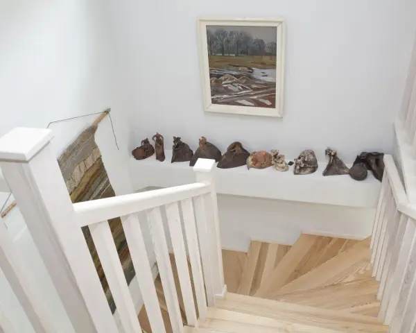 Klatka schodowa inspiracje: białe balustrady, drewniane stopnie i galeria ceramicznych rzeźb na półce.