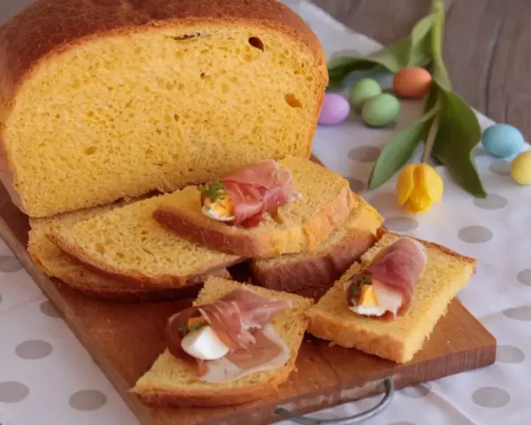 Fetta di torta al formaggio umbra ricetta originale, guarnita con prosciutto e uovo sodo. Uova colorate e tulipani sullo sfondo.