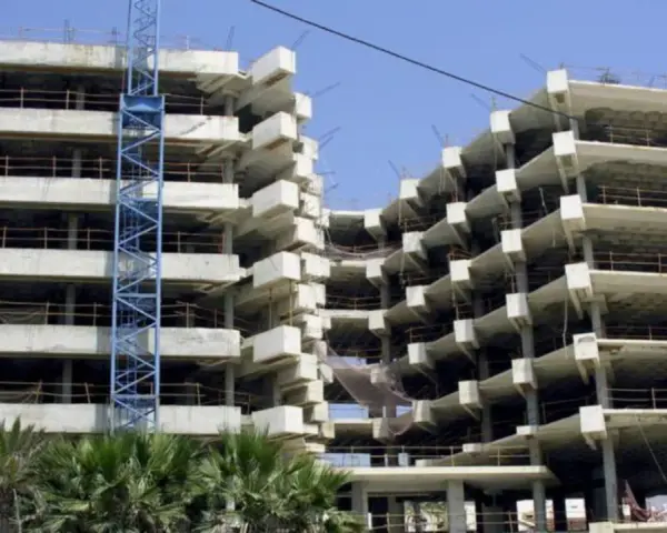 Edificio en construcción con grúa azul. La obra avanza lentamente, generando preocupación por sentencias de retraso en la entrega de vivienda de obra nueva.