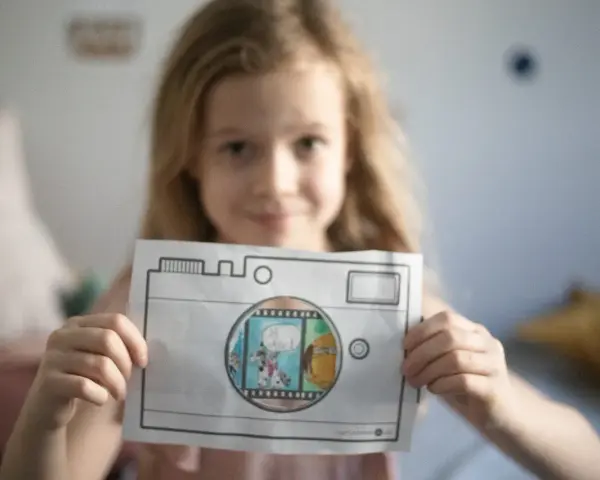 Uśmiechnięta dziewczynka pokazuje rysunek aparatu, przez który widać scenkę z pieskami. To świetna zabawa dla dziecka do lat 4 jak liczyć!