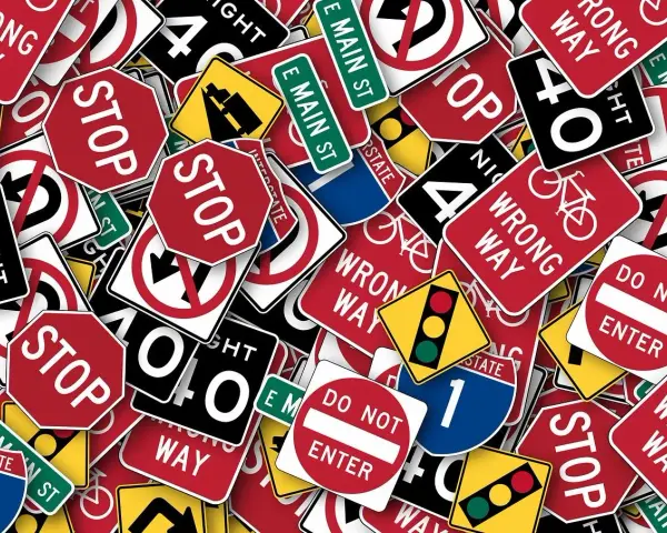 Un groviglio di segnali stradali, tra cui "STOP", "DO NOT ENTER" e "WRONG WAY", che ricordano l'art. 45 del Codice della Strada.