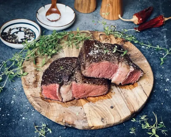 Zwei saftige Rib-Eye-Steaks, perfekt gegrillt, liegen auf einem Holzbrett. Mit Meersalz und Pfeffer bestreut, garniert mit frischem Thymian.
