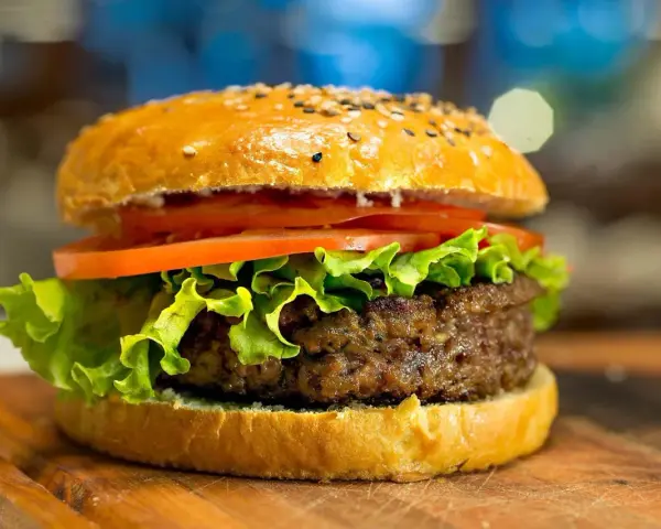 Apetyczny hamburger z sezamem, sałatą i pomidorem na desce.