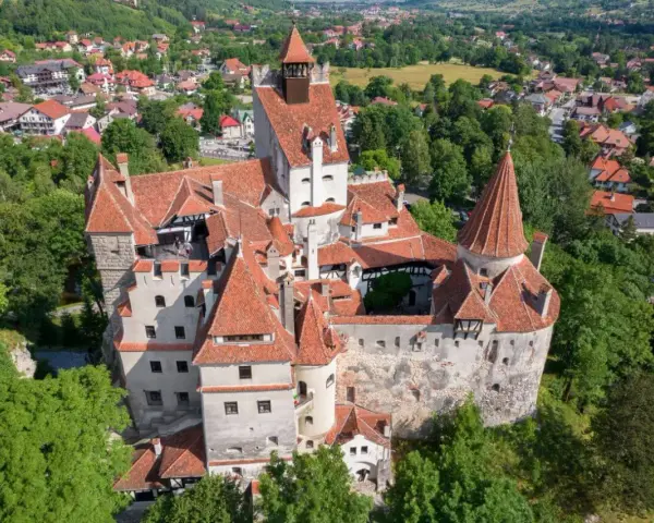 Dracula zamek, majestatyczna twierdza z czerwonymi dachami, otoczona zielenią i malowniczą wioską.