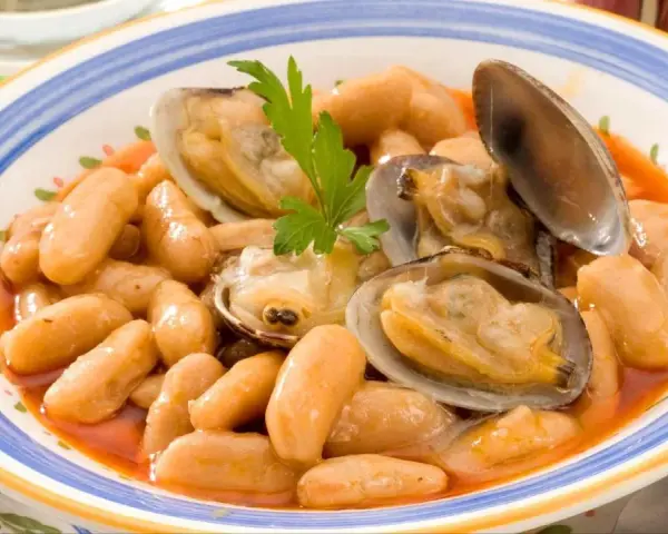 Plato de fabes con almejas, un guiso tradicional asturiano con judías blancas tiernas y jugosas almejas, decorado con perejil fresco.