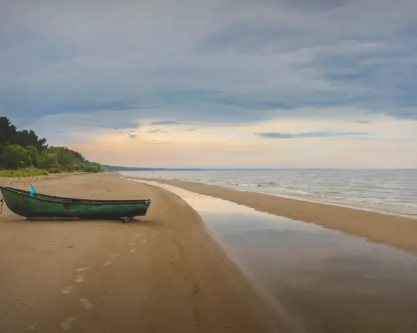 Zielona łódź na piaszczystej plaży Mierzei Wiślanej, idealne miejsce na camping. Woda odbija niebo, tworząc spokojny krajobraz.