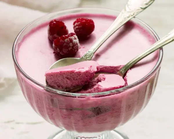 Himbeere-rotweincreme selbstgemacht in einer Glasschale, garniert mit frischen Himbeeren und zwei Löffeln.