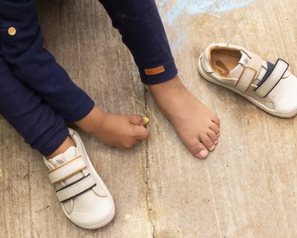 Niño descalzo dibuja con tiza junto a sus zapatos de calzado fisiológico, listos para la aventura.