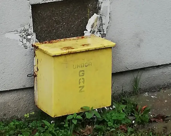 Żółta skrzynka gazowa w elewacji budynku, z napisem "UWAGA GAZ".