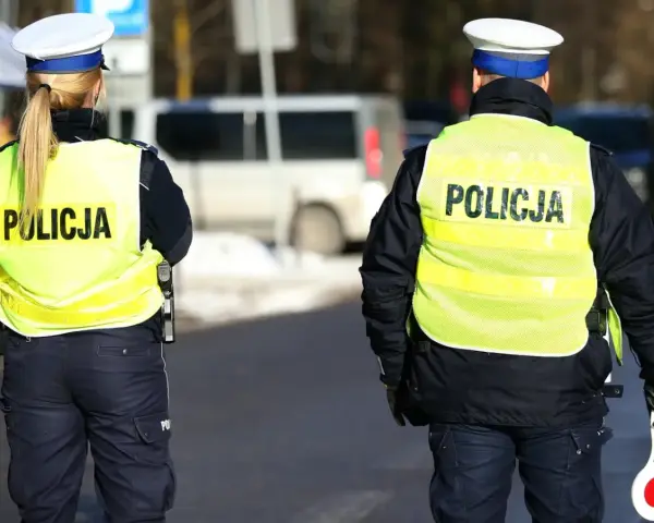 Dwóch policjantów w kamizelkach odblaskowych z napisem "POLICJA" stoi na drodze.