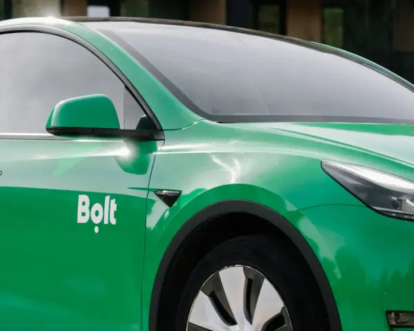Zielone auto z oklejeniem Bolt. Widoczna część drzwi, lusterko i fragment maski.