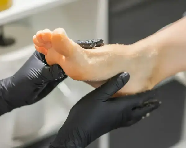 Dłonie w czarnych rękawiczkach wykonują peeling stopy. To właśnie jest pedicure co to znaczy pielęgnacja stóp.