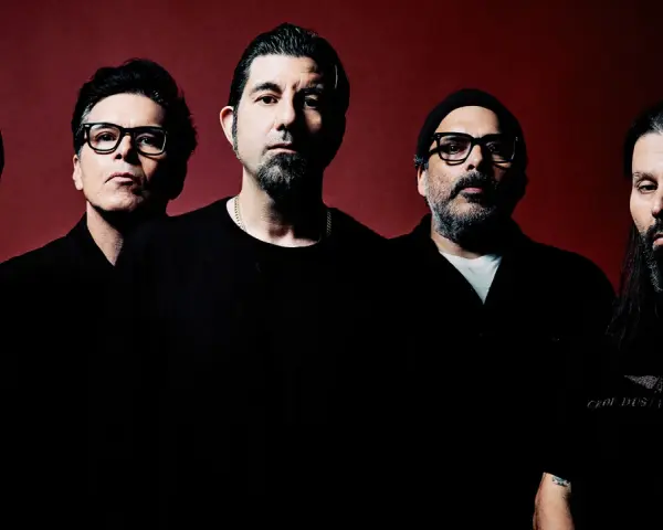 Pięciu mężczyzn, zespół Deftones Polska, pozuje do zdjęcia na ciemnoczerwonym tle.