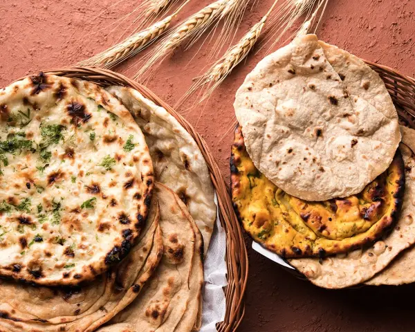 Dwa koszyki pełne pysznego chleba indyjskiego, w tym aromatyczny naan z kolendrą i klasyczny roti, ozdobione kłosami zboża.
