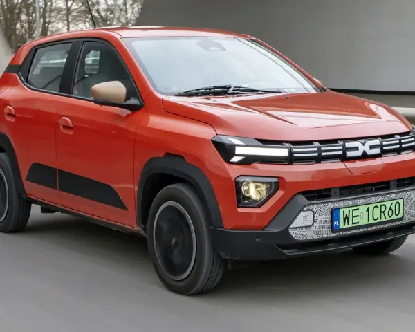 Pomarańczowy Dacia Spring, najtańsze auto elektryczne, jedzie po drodze.
