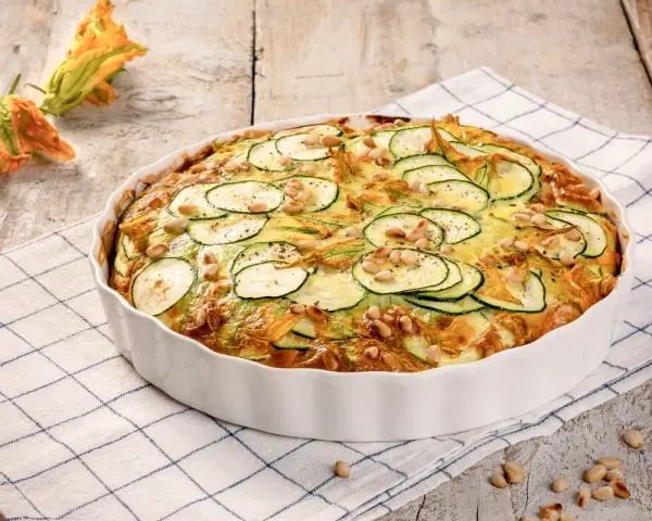 Frittata di zucchine al forno, guarnita con pinoli e fiori di zucca, pronta per essere gustata.