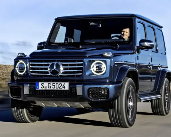 Ciemnoniebieski Mercedes G Klasa jedzie po pustynnej drodze. Kierowca uśmiecha się. Sprawdź mercedes g klasa cena!