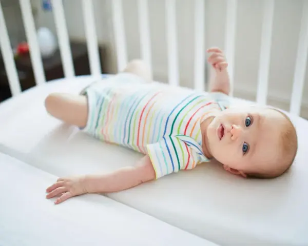 Niemowlę w kolorowym body leży w łóżeczku. Jego niebieskie oczy przypominają **perły Epsteina**, a uśmiech rozjaśnia pokój.