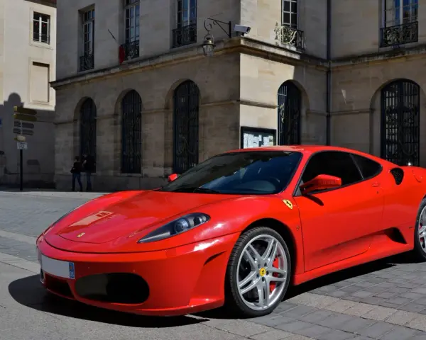 Czerwone Ferrari F430 zaparkowane na brukowanej ulicy przed kamienną kamienicą.