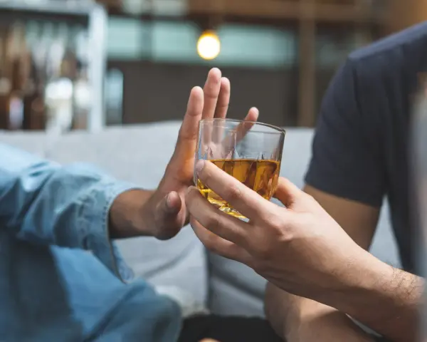 Dłoń odrzuca szklankę z alkoholem. Przykład asertywnego odmawiania picia alkoholu.