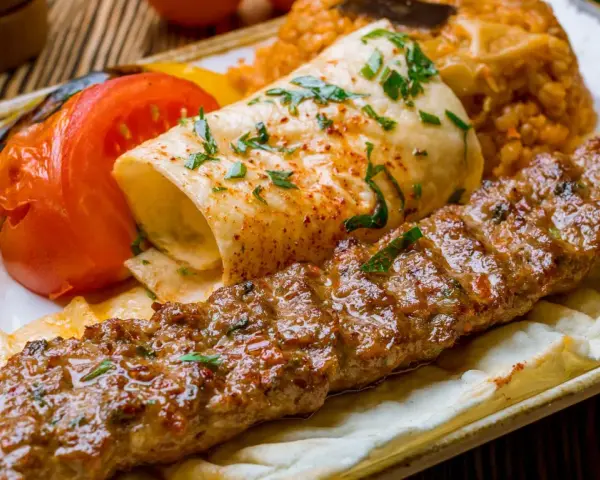 Kebab z mięsa mielonego, grillowane warzywa, placek i ryż na talerzu.
