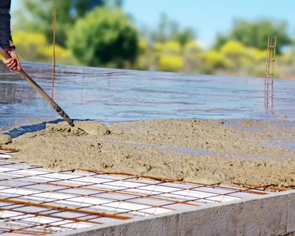 Coulée de béton frais sur une armature métallique pour assurer l'épaisseur dalle maison. Le travailleur étale le béton avec une pelle.