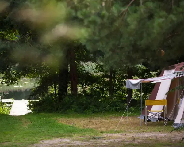 Namiot i krzesło na tle jeziora i lasu. Idealne pola namiotowe Mazury dla miłośników natury.