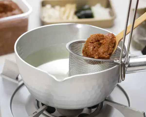Łyżka z pastą miso trafia do bulionu. Tak przygotowuje się bazę do zupy, pytasz miso co to? To fermentowana pasta sojowa.