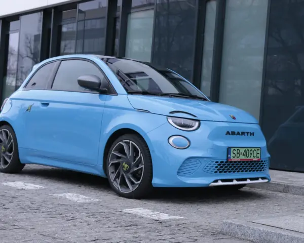Niebieski Abarth 500e, gotowy do testów, zaparkowany przed nowoczesnym budynkiem.