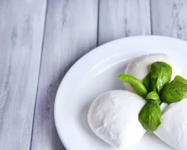 Trzy kulki serka mozzarella z listkami bazylii na białym talerzu. Idealne do sałatki, znasz ser mozzarella kcal?