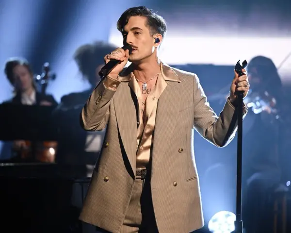 Un cantante con un completo gessato e camicia satinata, microfono in mano, incarna il **dandy significato** con stile sul palco.