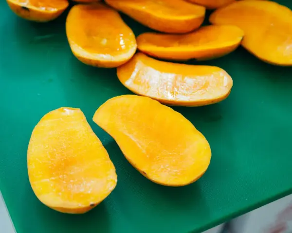Pokrojone w łódeczki, soczyste mango w intensywnym kolorze, jakby w ciąży z owocową obfitością, leżą na zielonej desce.