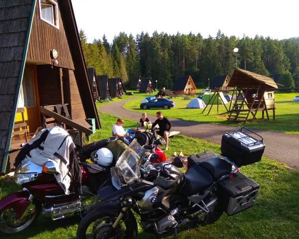 Motocykliści odpoczywają na kempingu w Rumunii, otoczeni drewnianymi domkami i lasem.