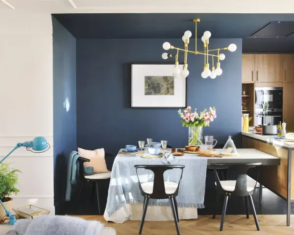 El azul oscuro combina con tonos pastel, madera y dorado. Un comedor elegante con mesa, sillas negras, lámpara dorada y flores.