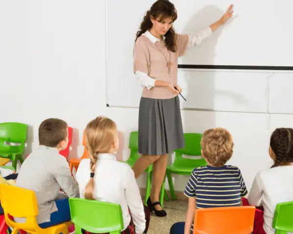 Nauczycielka prowadzi lekcję dla dzieci w klasie. To początek roku szkolnego w Hiszpanii, dzieci siedzą na kolorowych krzesełkach.