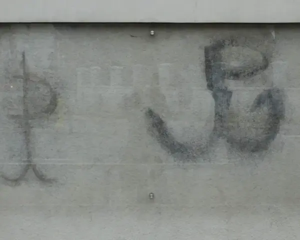 Na szarej ścianie widoczny jest symbol kotwicy, znak Polski Walczącej, namalowany czarną farbą.