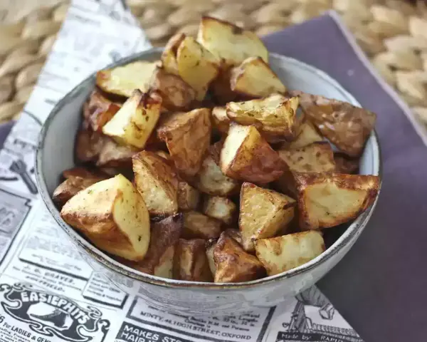 Patate dorate e croccanti in friggitrice ad aria, servite in una ciotola su carta di giornale.