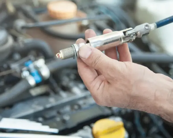 A hand holds a spark plug with a socket wrench attached, ready for a spark plug replacement. This DIY task can save on the spark plug replacement cost.