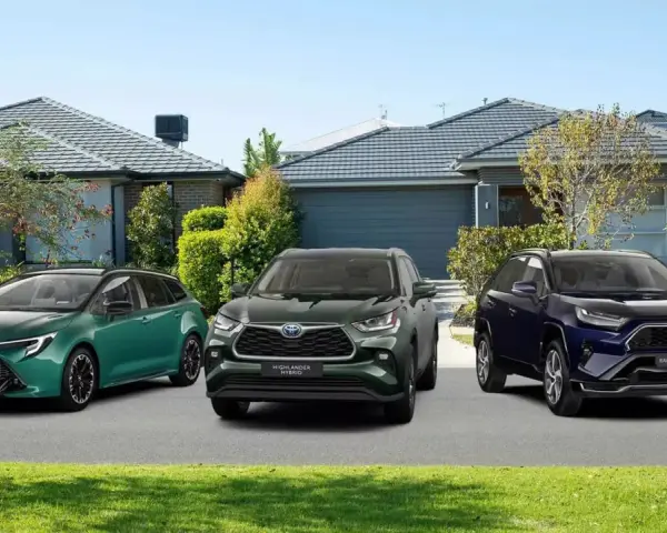 Trzy modele Toyota SUV: zielony kombi, ciemnozielony Highlander Hybrid i granatowy RAV4 Plug-in Hybrid, zaparkowane przed domami.