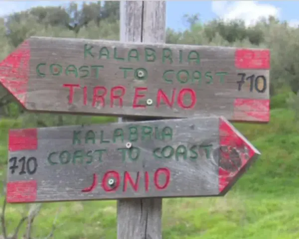 Cartelli in legno indicano il percorso "Kalabria Coast to Coast": uno punta a Tirreno, l'altro a Jonio.