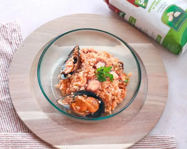 Delicioso arroz con pulpo y mejillones, servido en un cuenco de cristal sobre una tabla de madera.