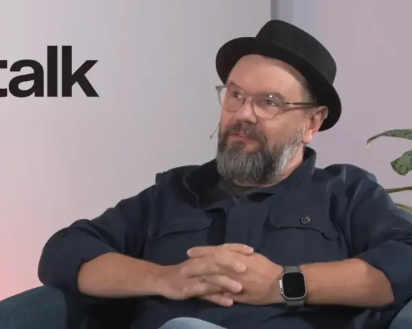 Mężczyzna w okularach i kapeluszu siedzi, rozmawiając. Obok logo DGP talk.