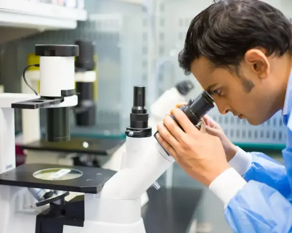 Mężczyzna w niebieskiej fartuchu laboratoryjnym bada próbkę pod mikroskopem, kluczowy element w diagnostyce patomorfologia.